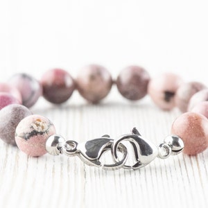 May include: A pink and white gemstone bracelet with a silver clasp. The bracelet is made of round beads and is approximately 7 inches in length.