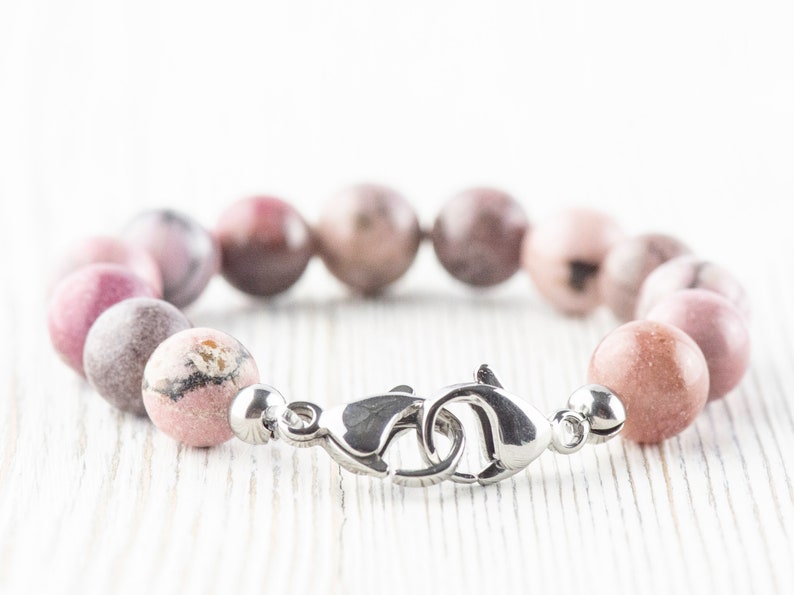 May include: A pink and white gemstone bracelet with a silver clasp. The bracelet is made of round beads and is approximately 7 inches in length.
