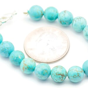 May include: A turquoise gemstone bracelet with a silver clasp. The bracelet is made of round beads with a marbled pattern. The beads are approximately the size of a UK 20 pence coin.