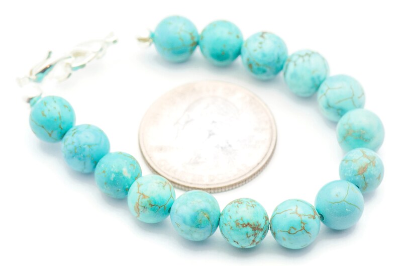 May include: A turquoise gemstone bracelet with a silver clasp. The bracelet is made of round beads with a marbled pattern. The beads are approximately the size of a UK 20 pence coin.