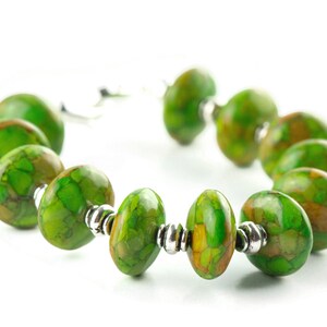 Pode incluir: Um bracelete de pedra verde e marrom com contas de prata. O bracelete &eacute; feito de pedras ovais com um padr&atilde;o de m&aacute;rmore.