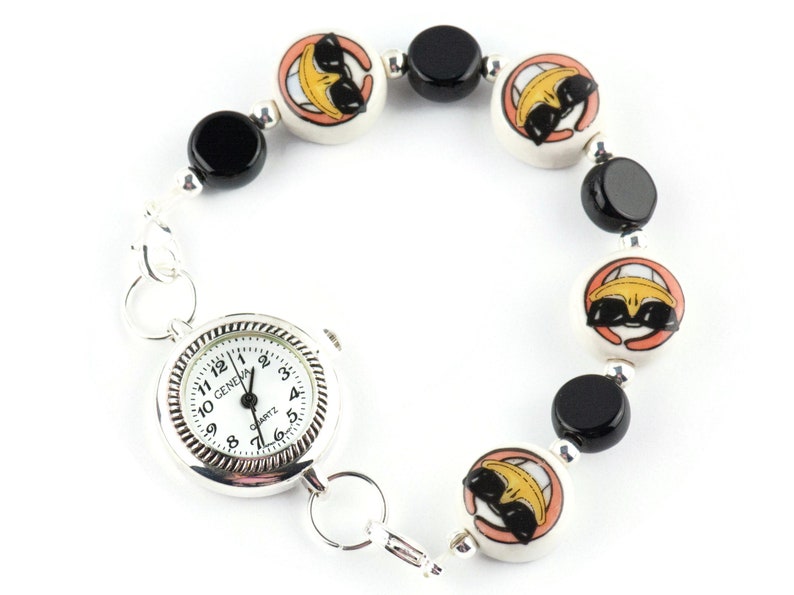 May include: A silver watch with a white face and black hands is attached to a bracelet made of black and white ceramic beads. The beads have a cartoon face with sunglasses on them.