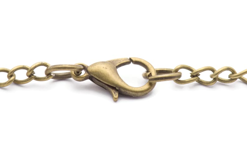Puede incluir: Primer plano de una cadena de collar de color bronce con un cierre de mosquet&oacute;n. Los eslabones de la cadena son de forma ovalada y el cierre tiene un dise&ntilde;o curvo. El metal tiene un aspecto vintage y antiguo.