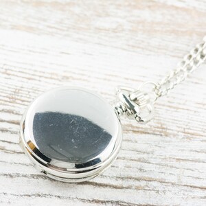 May include: A silver pocket watch with a chain on a white wooden surface.