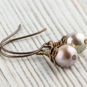 May include: A pair of pearl drop earrings. Each earring features a lustrous, off-white pearl suspended from a bronze-colored wire hook. The pearls have a subtle iridescent sheen, and the wire has a delicate, handcrafted appearance.