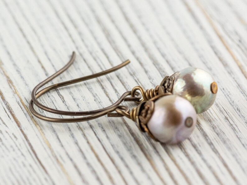 May include: A pair of pearl drop earrings. Each earring features a lustrous, off-white pearl suspended from a bronze-colored wire hook. The pearls have a subtle iridescent sheen, and the wire has a delicate, handcrafted appearance.