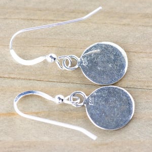 May include: A pair of silver dangle earrings with a round disc charm. The charms are stamped with "925" on the back.