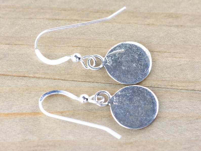 May include: A pair of silver dangle earrings with a round disc charm. The charms are stamped with "925" on the back.