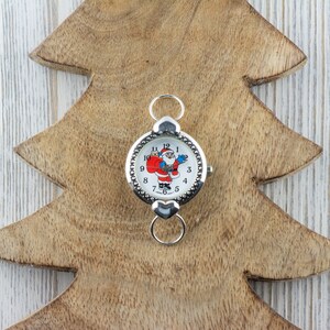 Peut inclure: Une montre argent&eacute;e avec un cadran blanc et un motif de P&egrave;re No&euml;l. La montre a une cha&icirc;ne argent&eacute;e et un fermoir.