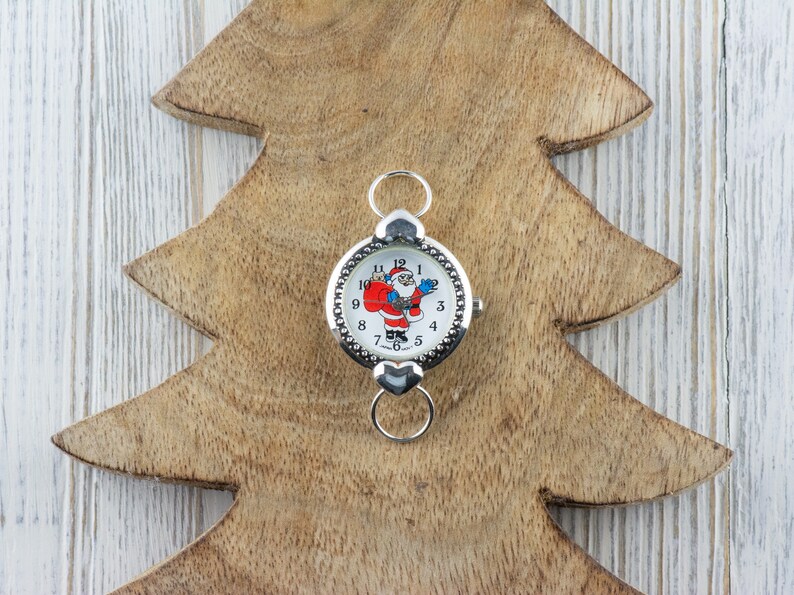 Peut inclure: Une montre argent&eacute;e avec un cadran blanc et un motif de P&egrave;re No&euml;l. La montre a une cha&icirc;ne argent&eacute;e et un fermoir.