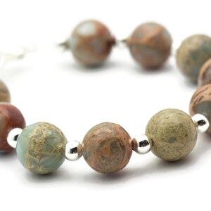 May include: A bracelet made of brown, green, and white marbled beads with silver accents.