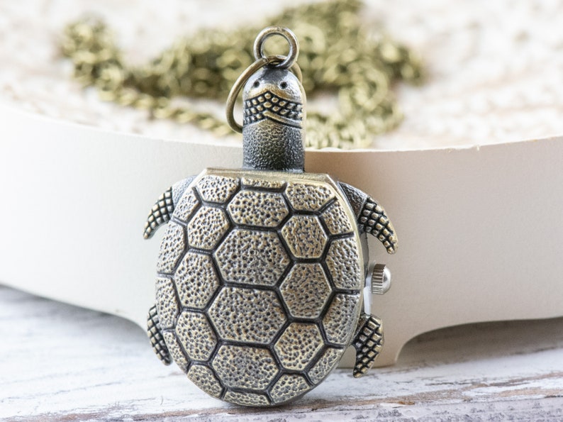 May include: A bronze turtle-shaped pocket watch pendant with a chain. The turtle has a detailed shell with hexagonal patterns.
