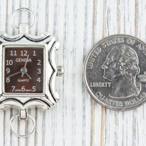 May include: A silver-toned watch with a square face and a brown dial. The watch is about the size of a US quarter. The watch face has black numbers and hands, and the words "GENEVA" and "QUARTZ" are printed on the dial.