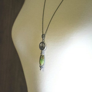 Puede incluir: Un collar de cadena de plata con un colgante de signo de paz y una cuenta verde y plateada.