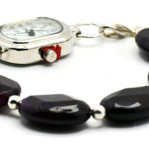 May include: A silver watch with a white face and black hands attached to a bracelet made of dark purple oval-shaped beads.
