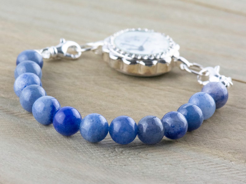 May include: A silver watch with a white face and a blue gemstone beaded bracelet.