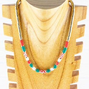 K&ouml;nnte beinhalten: Eine goldene Kettenkette mit roten, wei&szlig;en und gr&uuml;nen Perlen. Die Kette wird auf einer Holzpuppe pr&auml;sentiert.