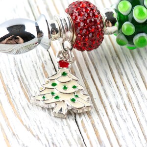 May include: A silver charm bracelet with Christmas-themed beads. The bracelet includes a charm in the shape of a Christmas tree with green and red accents. Other beads are red, green, and silver.