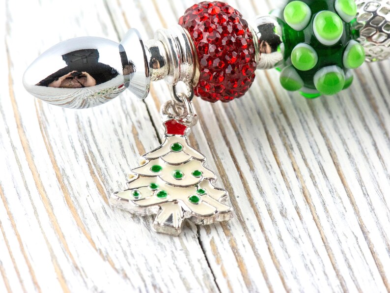May include: A silver charm bracelet with Christmas-themed beads. The bracelet includes a charm in the shape of a Christmas tree with green and red accents. Other beads are red, green, and silver.