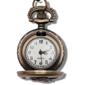 Puede incluir: Un reloj de bolsillo de estilo vintage con un acabado dorado antiguo y una esfera blanca. El reloj tiene marcadores de hora romanos negros y agujas negras. La esfera del reloj tambi&eacute;n incluye la palabra "QUARTZ" y marcas negras para los minutos.