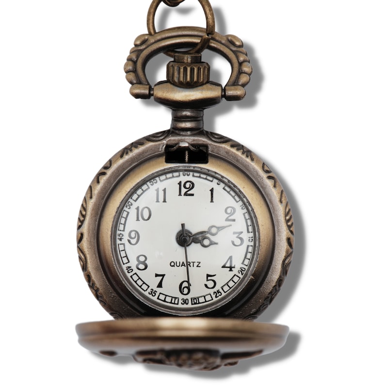 Puede incluir: Un reloj de bolsillo de estilo vintage con un acabado dorado antiguo y una esfera blanca. El reloj tiene marcadores de hora romanos negros y agujas negras. La esfera del reloj tambi&eacute;n incluye la palabra "QUARTZ" y marcas negras para los minutos.