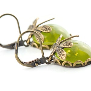 May include: A pair of green glass earrings with a dragonfly design. The earrings are made of brass and have a hook closure.