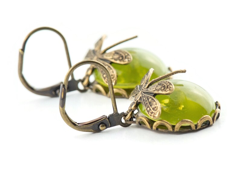 May include: A pair of green glass earrings with a dragonfly design. The earrings are made of brass and have a hook closure.