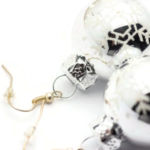 May include: A pair of silver Christmas ornament earrings with snowflake designs. The earrings are attached to gold-toned hooks.