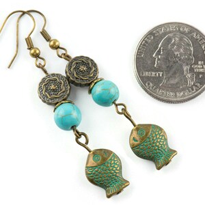 May include: Turquoise and bronze dangle earrings with a fish charm and a turquoise bead. The earrings are about the size of a quarter.