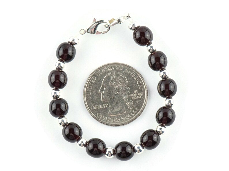 K&ouml;nnte beinhalten: Ein Armband aus dunkelroten Edelsteinen mit silbernen Perlen und einem silbernen Verschluss. Das Armband ist etwa so gro&szlig; wie eine 25-Cent-M&uuml;nze.