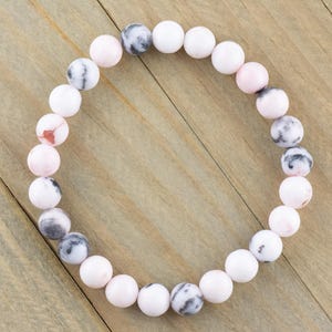 May include: A pink and white gemstone bracelet with round beads. The bracelet is made of natural stones and has a simple design.