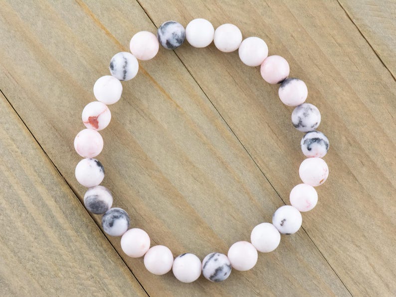 May include: A pink and white gemstone bracelet with round beads. The bracelet is made of natural stones and has a simple design.