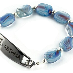 May include: A medical alert bracelet with a silver tag that reads "ASTHMA" and a star of life symbol. The bracelet is made of blue and white glass beads.