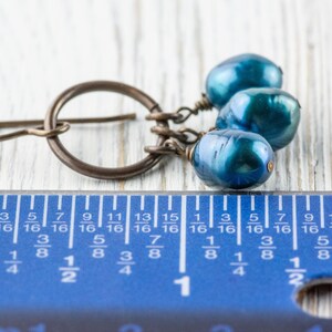 K&ouml;nnte beinhalten: Ein einzelner Ohrring mit einem bronzefarbenen Reifen und drei blau-gr&uuml;nen, birnenf&ouml;rmigen Perlen. Der Ohrring ist neben einem blauen Lineal, die L&auml;nge des Ohrrings betr&auml;gt ca. 1,9 cm.