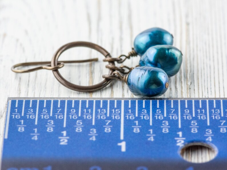 K&ouml;nnte beinhalten: Ein einzelner Ohrring mit einem bronzefarbenen Reifen und drei blau-gr&uuml;nen, birnenf&ouml;rmigen Perlen. Der Ohrring ist neben einem blauen Lineal, die L&auml;nge des Ohrrings betr&auml;gt ca. 1,9 cm.