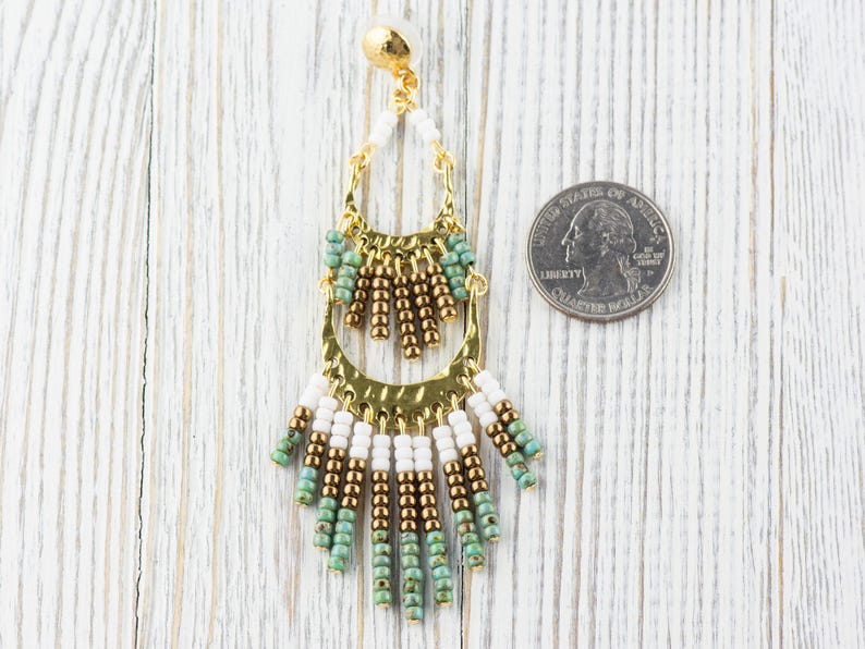May include: Gold tone dangle earrings with white, brown, and turquoise beads. The earrings are about the size of a US quarter.