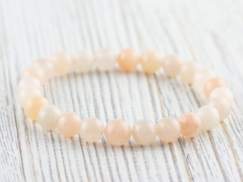 Op de afbeelding: Een armband gemaakt van lichtroze en witte ronde kralen. De armband ligt op een wit houten oppervlak.