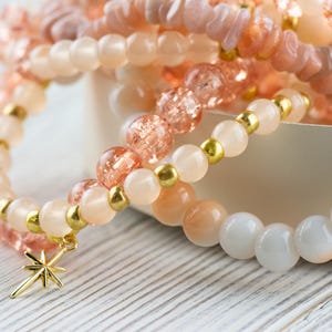 May include: A set of three bracelets featuring pink and white beads with gold accents. The bracelets have a star charm.