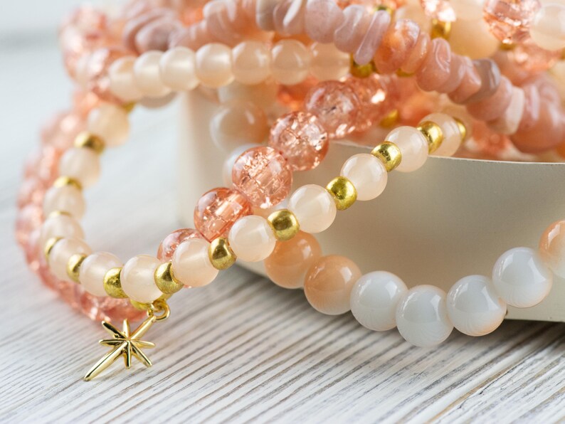 May include: A set of three bracelets featuring pink and white beads with gold accents. The bracelets have a star charm.