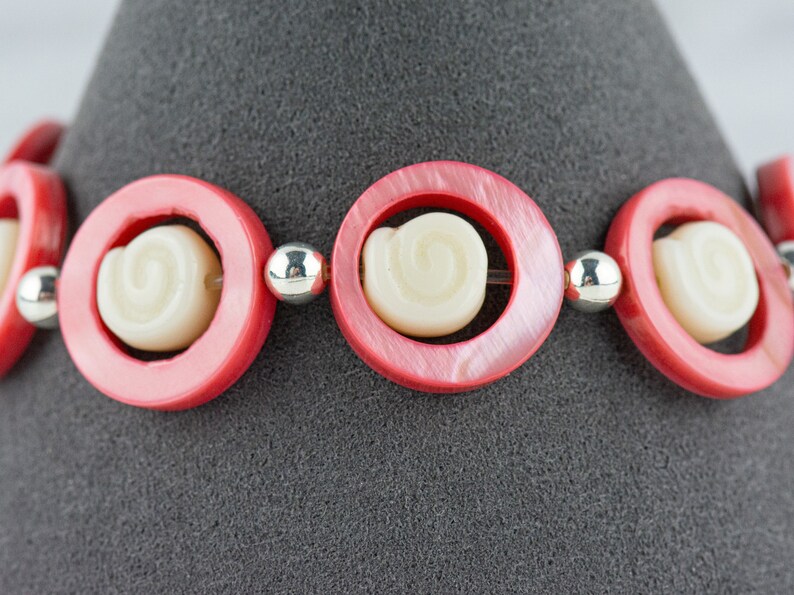 Pu&ograve; includere: Un braccialetto rosa e bianco con perline rotonde che presentano un design a spirale. Il braccialetto &egrave; realizzato in plastica e ha un accento in metallo argentato.