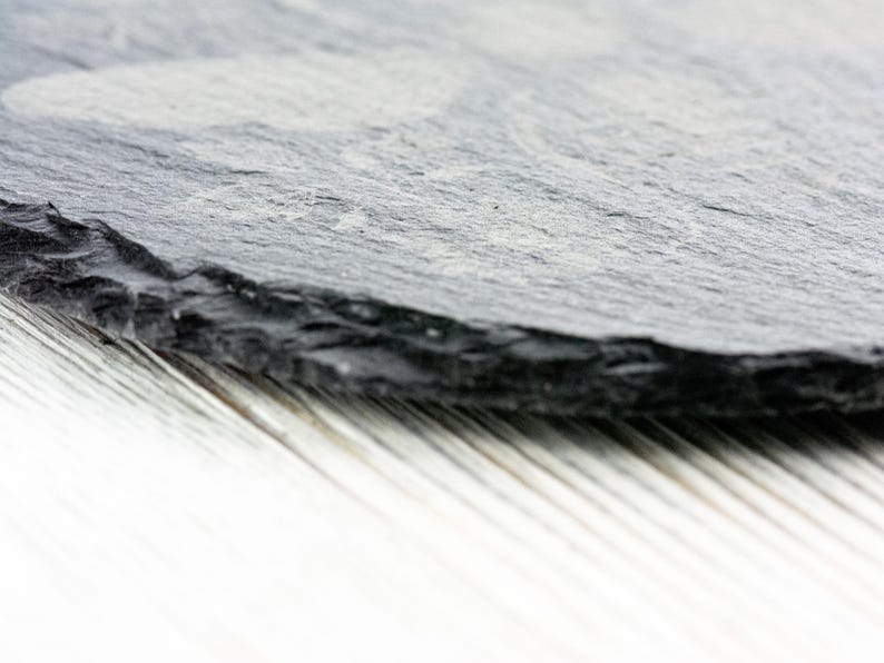 Op de afbeelding: Een close-up van een donkergrijze leisteen serveerschaal met een ruw, getextureerd oppervlak. De schaal is licht gekanteld en lijkt van natuursteen te zijn.