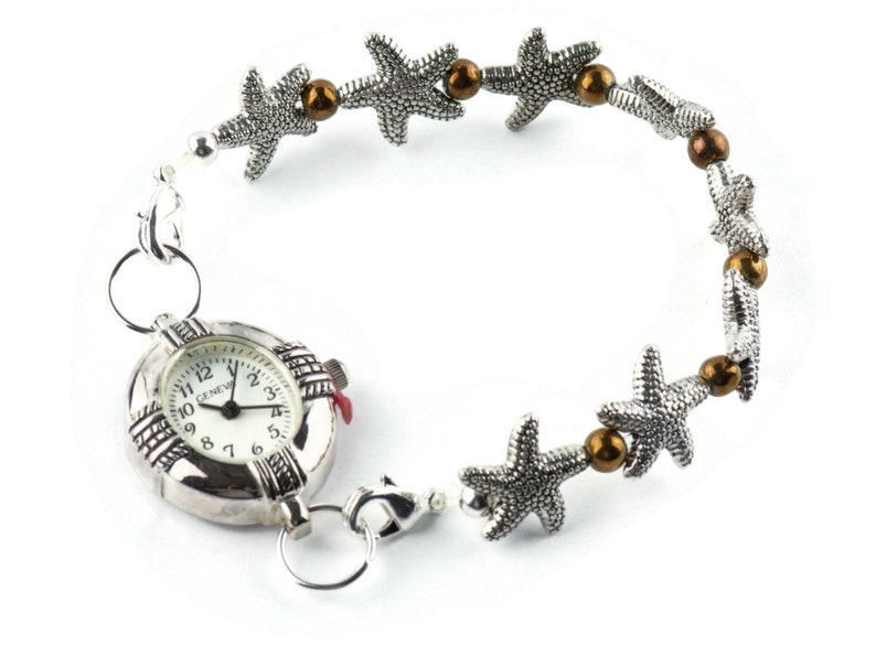 K&ouml;nnte beinhalten: Eine silberne Uhr mit einem runden Zifferblatt und r&ouml;mischen Ziffern. Die Uhr ist an einer silbernen Kette mit braunen Perlen und silbernen Seestern-Anh&auml;ngern befestigt.