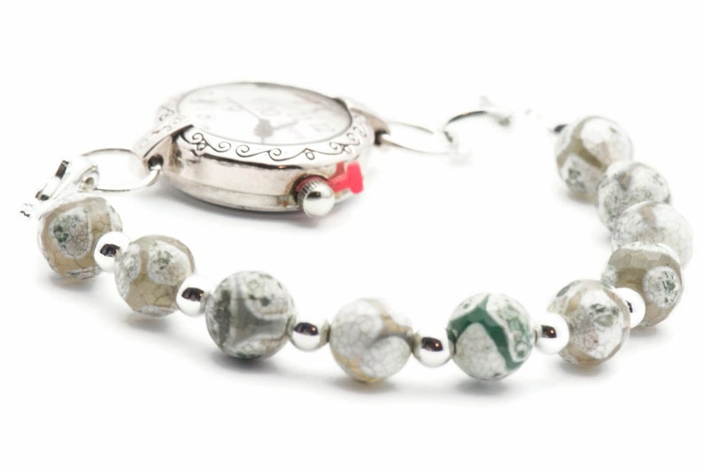 Op de afbeelding: Een zilveren horloge met een witte wijzerplaat en zwarte wijzers is bevestigd aan een armband gemaakt van grijze en groene agaat kralen.