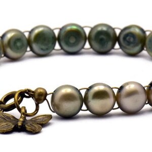 Op de afbeelding: Een armband gemaakt van groene en bruine parels met een bronzen vlinderbedel.