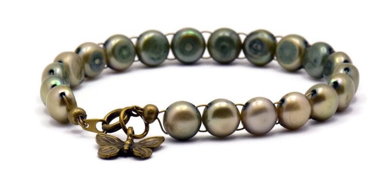 Op de afbeelding: Een armband gemaakt van groene en bruine parels met een bronzen vlinderbedel.