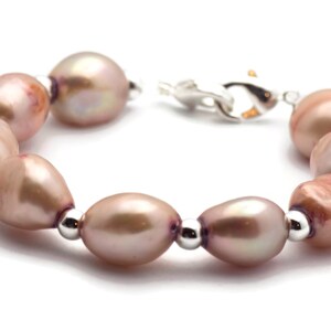 May include: A bracelet made of light pink oval pearls with silver accents. The bracelet has a silver clasp.