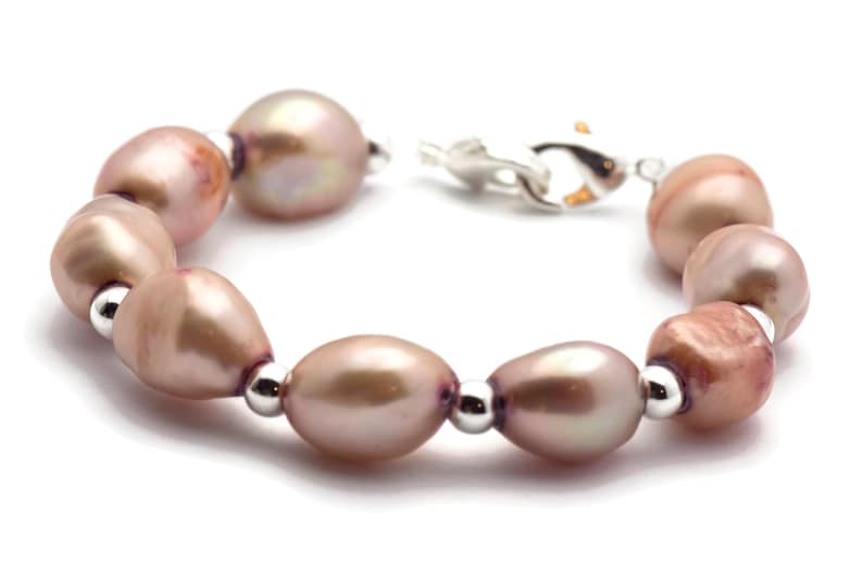 May include: A bracelet made of light pink oval pearls with silver accents. The bracelet has a silver clasp.