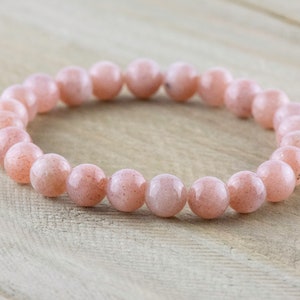 May include: A pink sunstone beaded bracelet with a natural, earthy look. The bracelet is made of round beads and is approximately 7 inches in length.