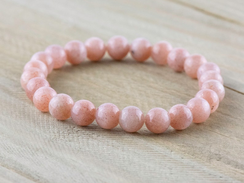 May include: A pink sunstone beaded bracelet with a natural, earthy look. The bracelet is made of round beads and is approximately 7 inches in length.