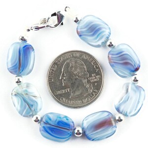 May include: A blue and white glass bead bracelet with a silver clasp. The bracelet is about the size of a quarter.